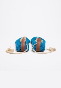 Blauwe gehaakte schoenen met bruine leren accenten en beige touwveters, met een gestructureerd oppervlak en een ronde vorm.