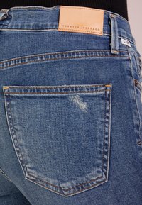 Denim jeans in medium blue with a slight distressed pattern. Features a leather label marked "PREMIUM VINTAGE" and detailed stitching.