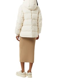 Dikke crèmekleurige jas met capuchon, ribgebreide beige rok en witte sneakers. Focus op zachte texturen en gestructureerde vormen.