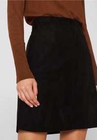 Schwarzer Wildleder-Minirock mit glatter Textur, hoher Taille und minimalen Nahtdetails, kombiniert mit einem braunen gerippten Pullover.