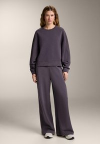 Felpa oversize in misto cotone di colore viola con maniche ampie, abbinata a pantaloni a gamba larga coordinati. Accentuata da una vestibilità confortevole, dallo stile casual.