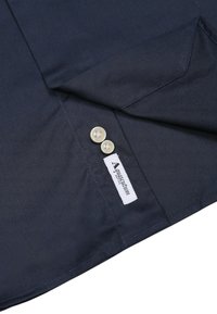 Tessuto di camicia blu navy, con colletto a bottoni dotato di due bottoni bianchi, e un'etichetta con la scritta "AquaScrutum" vicino alla cucitura.