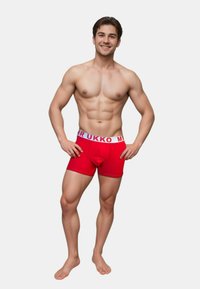 Röda kalsonger med vit midja som har texten "MR UKKO". Tyget ser ut att vara stretchigt och åtsittande, med en blank yta.