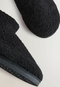 Papuci negri, din material pufos, cu un exterior texturat și un vârf rotunjit. Sole groase din cauciuc oferă aderență, accentuând un design confortabil, de interior.