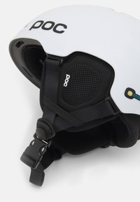 Weißer POC-Skihelm mit verstellbarem schwarzem Kinnriemen, gepolsterten Ohrenabdeckungen und Belüftungsnetz, auf einem weißen Hintergrund dargestellt.