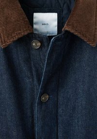 Jeans jakna z rjavim kordurovim ovratnikom, temno modrim materialom, dvema sprednjima gumboma in podloženim prešitim podlogom. Vidna etiketa znotraj.