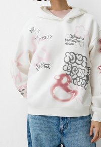 Felpa bianca con cappuccio caratterizzata da diverse stampe grafiche in rosa, nero e grigio, inclusi testi e disegni, tessuto testurizzato e polsini a coste.