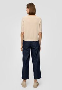 Beige Kurzarmpullover mit entspannter Passform, kombiniert mit dunkelblauen weiten Jeans und hellen klobigen Schuhen.