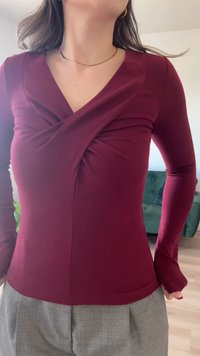 Top de manga larga color burdeos con un diseño retorcido en el escote. La tela es suave y ajustada, con un ligero brillo, combinada con pantalones grises.