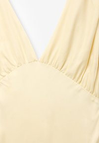 Robe sans manches jaune avec un décolleté en V profond et une taille froncée. Le tissu est lisse et légèrement extensible. Design simple et minimaliste.