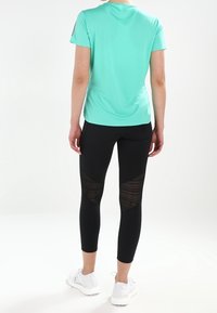 Una camicia verde menta a maniche corte è abbinata a leggings neri con un motivo a rete testurizzata sulle gambe inferiori. Scarpe da ginnastica bianche completano il look.