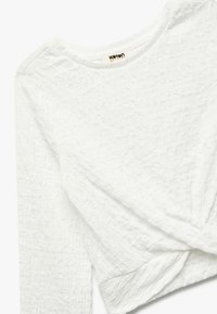 Hvid tekstureret langærmet top med en rund halsudskæring og en knude detalje ved kanten. Lavet af let, krøllet stof.