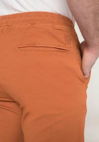 Oranga bomullsshorts med elastisk midja och en bakficka med klaff. Tyget är lätt och slätt i texturen.