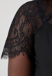 Black dress with lace overlay on short sleeves, featuring floral and circular patterns, textured edges, and a smooth body fabric.