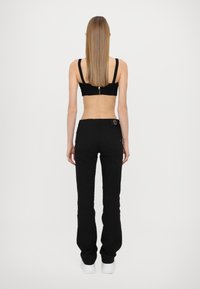 Black denim pants with a fitted silhouette, straight legs, and back pockets. Paired with a black cropped top, showcasing a zipper detail.