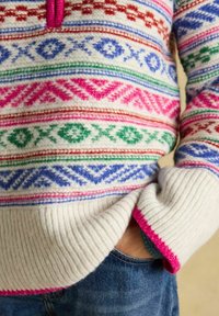 Strickpullover mit weißem Grund, der mehrfarbige geometrische Muster in Pink, Grün, Blau und Rot aufweist. Gerippte Bündchen mit pinken Akzenten.
