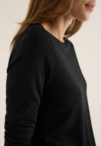 Schwarzes Langarmshirt aus weichem, strukturiertem Stoff mit dezentem metallischem Schimmer, Rundhalsausschnitt und taillierter Silhouette.