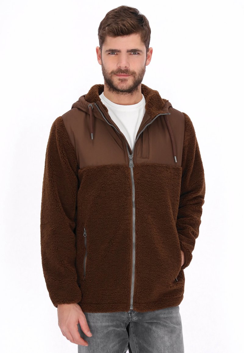Chaqueta marrón peluda con un panel liso marrón en el pecho, cremallera frontal y capucha. Cuenta con dos bolsillos laterales para almacenamiento.
