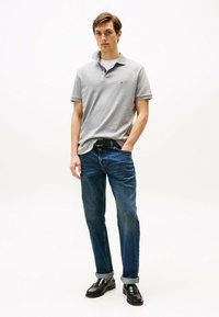 Grijze katoenen polo shirt met korte mouwen, gecombineerd met donkerblauwe spijkerbroek. De outfit wordt aangevuld met zwarte instappers.