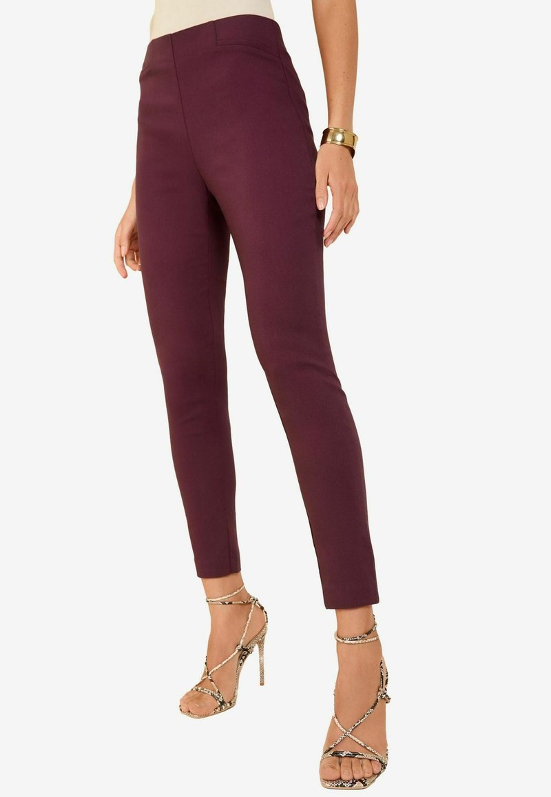 Pantalons ajustés bordeaux avec une taille haute, texture lisse et longueur cheville. Associés à des sandales à talons hauts en métal avec des brides.
