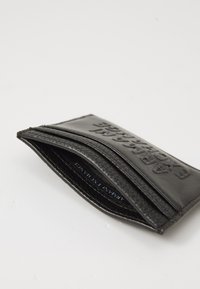 Juodas odinis kortelių laikiklis su įspaustu tekstu "ARMANI EXCHANGE", pasviręs ant balto fono, rodo kelis kortelių lizdus.