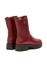 Botines de cuero rojo hasta el tobillo con cremallera lateral, suela de goma, punta redondeada y costuras decorativas. Presenta una pequeña etiqueta con el logo y una lengüeta de tirón.