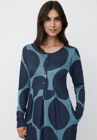 Abito a maniche lunghe blu navy e teal con grandi motivi circolari, scollo rotondo, chiusura con bottoni e tasche laterali. Tessuto morbido e texture.
