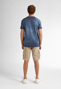 Tmavě modrá texturovaná košile s krátkým rukávem a kulatým výstřihem, v kombinaci s béžovými cargo šortkami s bočními kapsami a bílými teniskami.