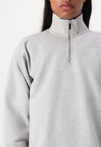 Szürke cipzáras sweatshirt magas gallérral, puha anyagból készült, rövid cipzárral és hosszú ujjal. Sima textúra.
