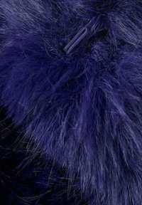 Primo piano di un colletto in pelliccia sintetica blu scuro con un pulsante a loop intrecciato visibile per la chiusura di un cappotto o giacca.