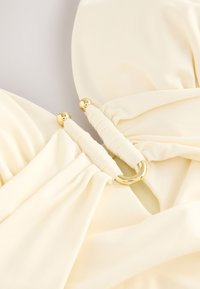 Creamy yellow fabric with gathered texture, featuring gold hardware accents and elastic loops for secure fastening.