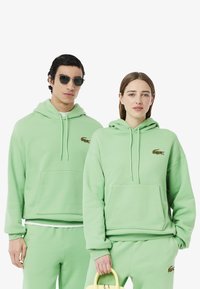 Felpe verde menta con tasche a marsupio e cappucci con coulisse, caratterizzate da un piccolo logo ricamato. Tessuto morbido, design unisex.