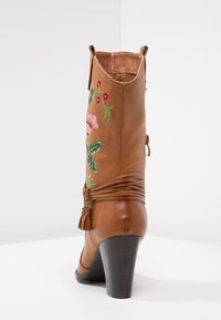 Brauner Kunstleder-Stiefel mit hohen Absätzen, floralem Stickerei, dekorativen Fransen und einer strukturierten Oberfläche, der eine konturierte Form aufweist.