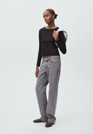 Zwarte lange mouw aansluitende top gecombineerd met grijze wijde jeans met geperforeerde details en vlakke bruine schoenen met versieringen.