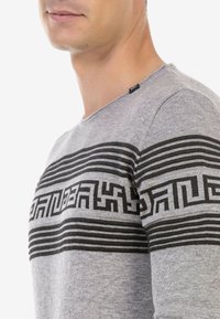 Grauer Pullover mit einem grafischen schwarzen Muster, horizontalen Streifen und geometrischen Designs, Rippenkragen und weicher Textur.