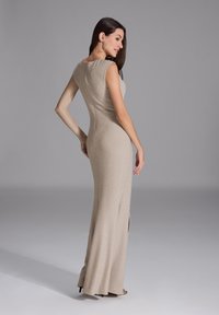 Muotiin mukautuva, hihaton iltapuku metallinhohtoisessa kullassa. Ominaisuuksiin kuuluu korkea halkio sivulla, sileä pinta ja se ulottuu lattiaan saakka.