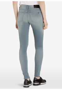 Jeans ajustados en denim azul claro, con bolsillos traseros, un ligero desvanecimiento y una cintura de altura media. Combinados con zapatillas deportivas negras.