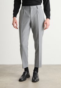 Gray tailored trousers with pleats, a slim fit, and a smooth texture, paired with black leather shoes and black socks.