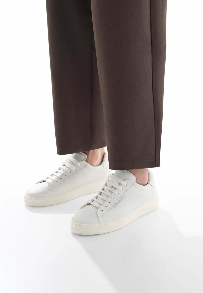 Sneakers in pelle bianca con suole in gomma piatte, punta rotonda e cuciture tonali. Le scarpe hanno sei coppie di occhielli per i lacci e un branding minimale.