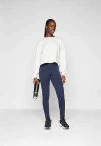Lys grå, avkortet langermet topp, marineblå leggings, svarte treningssko og en svart vannflaske, satt mot en enkel hvit bakgrunn.