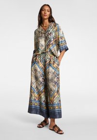 Paternované dvoudílné sety sestávající z krátkosrstého topu a volných kalhot v pestrém hedvábí, s kombinací květinových a geometrických vzorů.