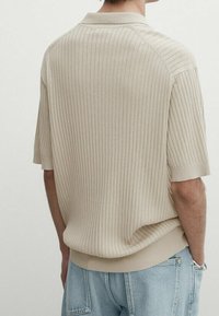 Beige ribbattu polo-paita pehmeällä tekstuurilla, jossa on kaulus ja lyhyet hihat, yhdistettyinä vaaleansinisiin farkkuihin.