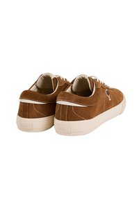 Sneaker in suede marrone con cuciture bianche, suole in gomma bianca e lacci, viste da dietro e da angolazioni laterali.