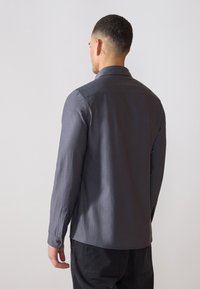Camicia da uomo a maniche lunghe di colore grigio scuro, realizzata in tessuto liscio. Caratterizzata da un colletto classico, polsini con bottone e un orlo dritto.