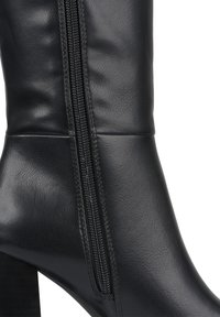 Bottine en cuir noir avec zip latéral, texture lisse, design sobre et semelle épaisse pour plus de stabilité.