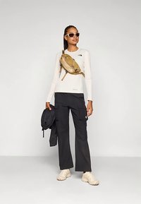 Langærmet hvid top, sorte cargobukser, tan farvet taljepose og beige sneakers. Tilbehør inkluderer hvide solbriller og en sort jakke.