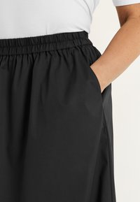 Black skirt with an elastic waistband, side pockets, smooth texture, and a relaxed silhouette, featuring a simple design with no embellishments.