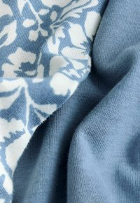 Közelkép puha, kék kötött anyagról fehér virágmintákkal, amely bemutatja a textúrát és az enyhe redőket.