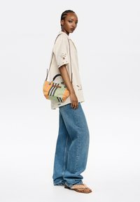 Colorful handbag with orange, green, and black stripes, paired with a light beige shirt featuring lace details and wide blue jeans.