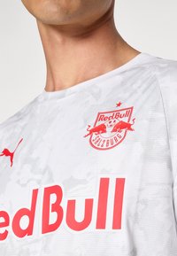 White short-sleeve sports jersey features a camouflage pattern, Puma logo, and large red "Red Bull" text with a circular club emblem.